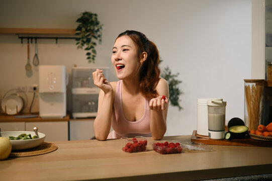 Young Asian Woman Enjoying Fresh Raspberries for Antioxidants Skin Nourishment and Anti Aging Benefits in Kitchen