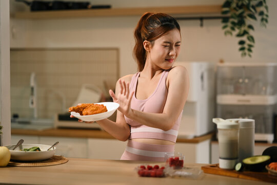 Young Asian Woman in Sportswear Refusing Fried Chicken on Diet, Healthy Eating Concept in Kitchen