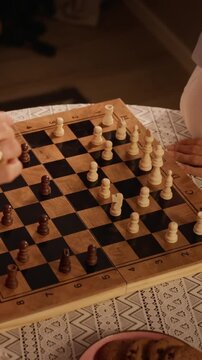 Vertical video of senior Caucasian woman and caregiver playing chess with wooden pieces. Footage perfect for geriatric healthcare and assisted living promotions