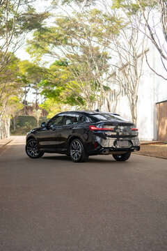 Black BMW X4 Luxury SUV Coupe Rear Three-Quarter View Parked On Tree-Lined Asphalt Road