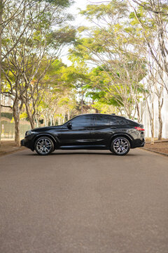 Black BMW X4 Luxury SUV Side Profile Parked On Tree-Lined Asphalt Road