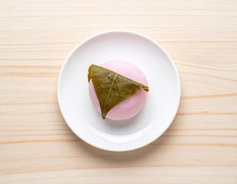 白い小皿に載せた桜の葉で包まれたピンク色の桜餅を真上から撮影した和菓子
