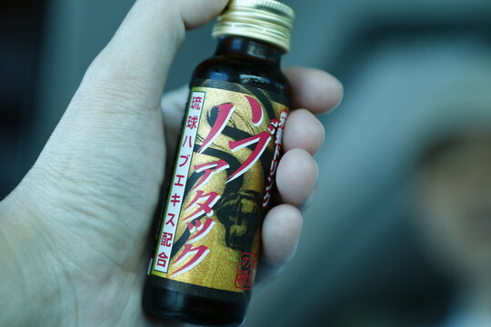 A hand holds a bottle of Habu snake energy tonic drink.