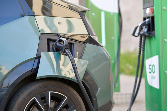 Minsk, Belarus. May 15, 2024. Closeup of green Zeekr electric car plugged into 50kw charging station with thick black cable, charging port and 50 kw fast charger Malanka by Belarusneft in background