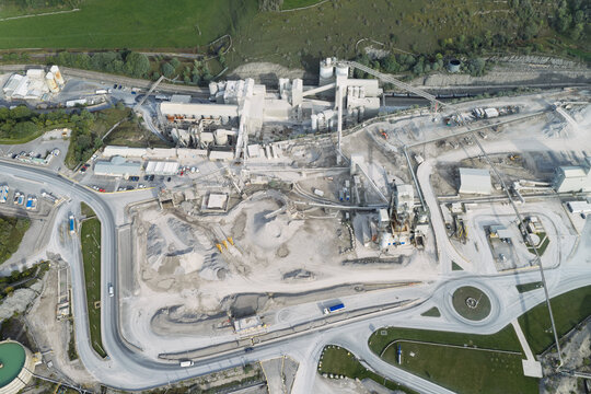 Aerial view of a large industrial cement plant featuring tall silos, processing buildings, conveyor belts, and a surrounding road network in the United Kingdom.