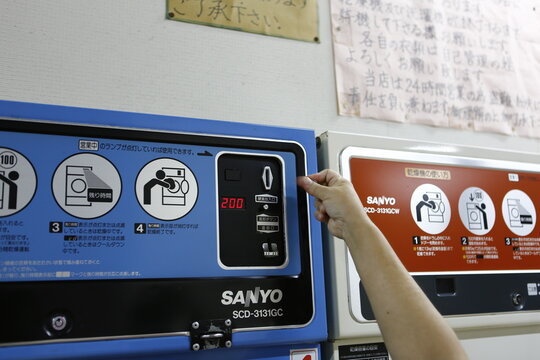 A customer inserts a coin into the control panel slot of a commercial dryer in a laundromat.