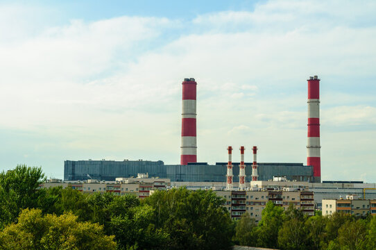 Industrial landscape background with tall red and white striped chimneys rising above a power plant and residential buildings