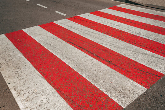 High-angle view of a red and white zebra pedestrian crosswalk painted on a asphalt street surface.