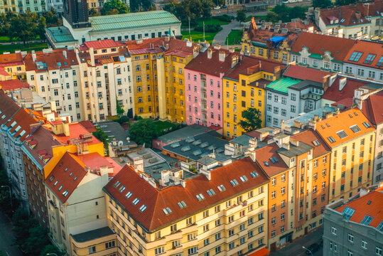 Dense historic cityscape of Prague illuminated by warm afternoon sunlight, with terracotta rooftops, traditional European buildings.