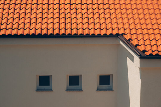 Three square windows lined up on a neutral stucco building wall under an orange terracotta tile roof.