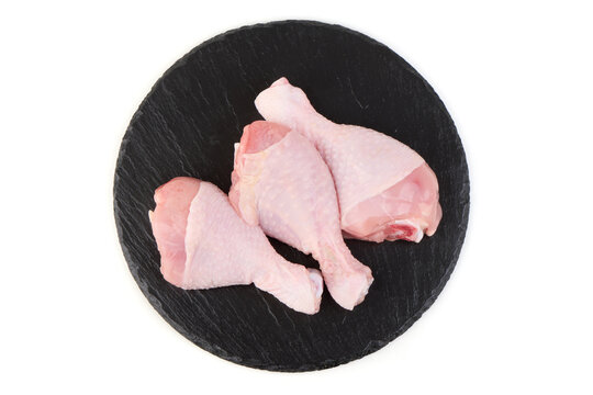 Raw chicken drumsticks on a black slate board