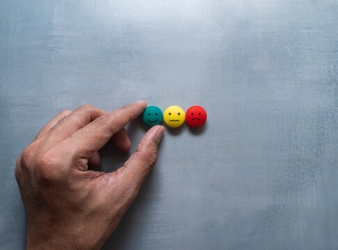 Hand selecting a green smiling face from green, yellow, and red emotion symbols on a gray background. Customer feedback, satisfaction ratings, quality, positive experience concept.