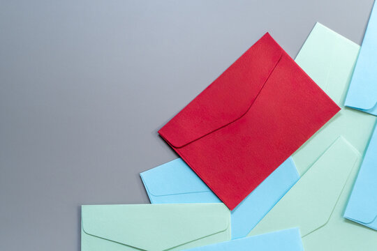 Red envelope on top a pile of blue and green envelopes on a gray background with copy space. Priority mail, urgent message, important notice, direct marketing concept.