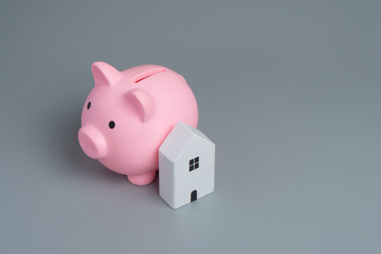 Piggy bank and a miniature house on a gray background with copy space. Home savings, mortgage planning, property investment, housing affordability, down payment concept.