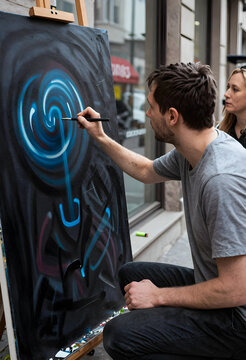 Creativity and artistic expression, male artist painting abstract blue spiral on large canvas in urban street setting with observer in background