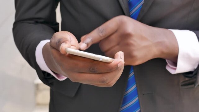 Closeup of a 20s young adult black African businessman's hand using a smartphone outdoors in an urban office setting, real human hand movement, front view