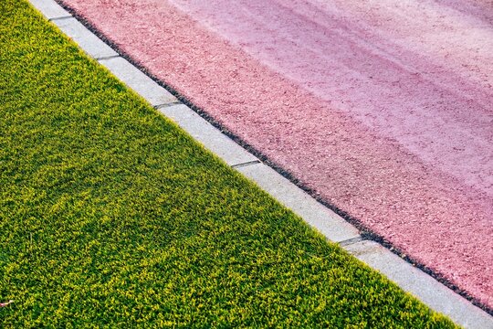 Vibrant green artificial grass next to a pink gravel pathway, closeup of contrasting landscaping textures and decorative outdoor ground surfaces