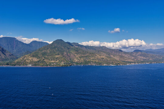 Aerial view of Amed Beach with lush green mountains, coastline, and deep blue sea in Bali, Indonesia.