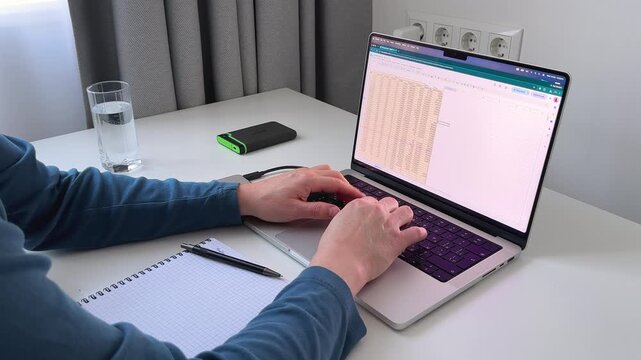 Man working on laptop analyzing data on spreadsheet in clean home office, side over the shoulder view, 4K video