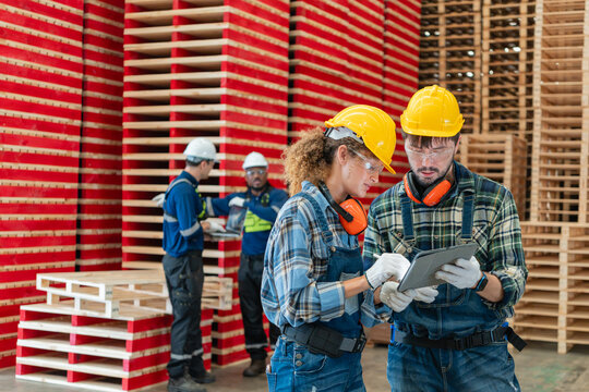 Tablet: a woman reviews carpentry workshop data as a female carpenter beside her colleague and two coworkers using a laptop.