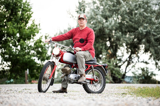 Portrait of a Senior Man Sitting on a Vintage 1970s European Motorcycle Looking at the Camera