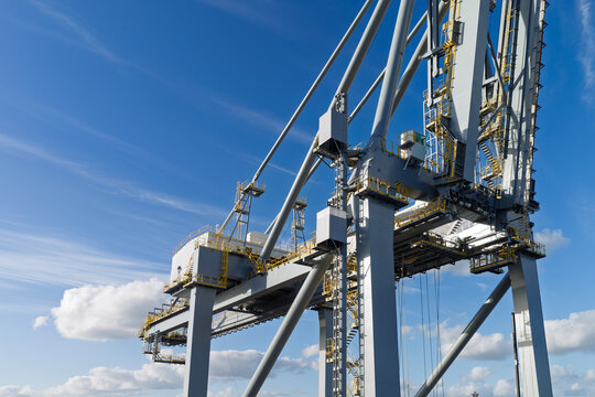 Aerial view of a large industrial gantry crane at a port facility under a clear blue sky in the United Kingdom.