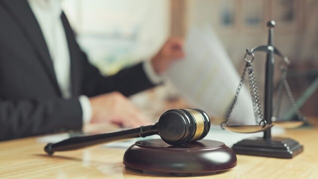 Wooden gavel balance scale rest on desk while attorney reviews legal contract documents. Legal consultation service, courtroom litigation justice system, corporate law compliance counsel.
