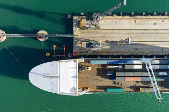Aerial view of a large cargo ship docked at a port terminal with industrial cranes and shipping containers in the United Kingdom.