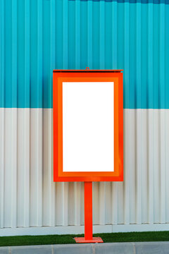 Blank rectangular sign on top of metal pole standing near colorful wall outdoors