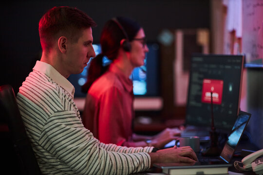 Young adult Caucasian man and woman working on computers in cybersecurity office, monitoring network threats. Useful for cyber defense, IT support and data protection campaigns