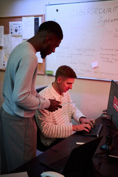 Vertical shot of young adult African American and Caucasian colleagues analyzing cybersecurity data on computer, representing IT security solutions for corporate advertising