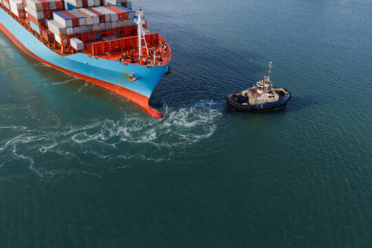 Aerial view of a large container ship being guided by a tugboat in the open sea, United Kingdom.