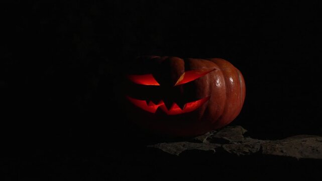 Light gradually fading on glowing carved jack o lantern resting on rustic stone wall at night, 4k 120fps super slow motion handheld footage