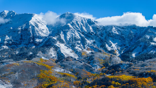 Aerial view of Ruby Peak Kebler Pass in Gunnison National Forest featuring snow-capped mountain peaks and vibrant autumn aspen forests with golden foliage in Crested Butte, Colorado, United States.