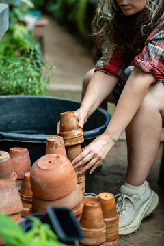 Focused female greenhouse employee preparing inventory for plants , stacking washed pots beside tub, focused woman florist plant nursery worker neatly organizing pots, daily routine work in orangery.