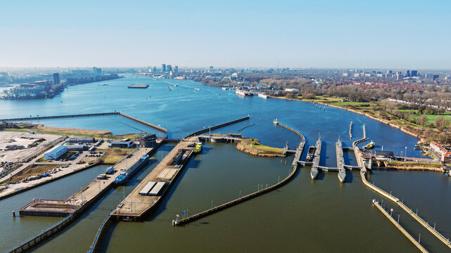 Aerial view of the Oranjesluizen lock complex with concrete walls, calm water, and industrial barges, with the city skyline in the distance in Amsterdam, North Holland, Netherlands.
