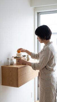 Woman arranging Kagami Mochi a traditional Japanese New Year decoration on a wooden shelf