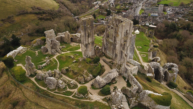 Aerial view of the historic ruins of Corfe Castle, featuring stone walls and towers set amidst green hills and the village of Corfe Castle, England, United Kingdom.