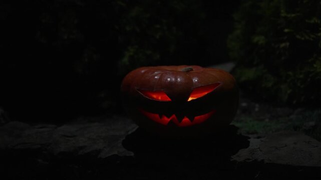 Illuminated carved jack o lantern on stone wall with moving light source and shifting shadows at night, 4k 120fps super slow motion footage