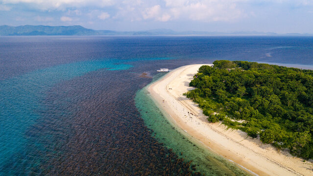 Aerial view of a tropical island with a white sand beach, lush green forest, and clear turquoise waters in Busuanga, Mimaropa, Philippines.