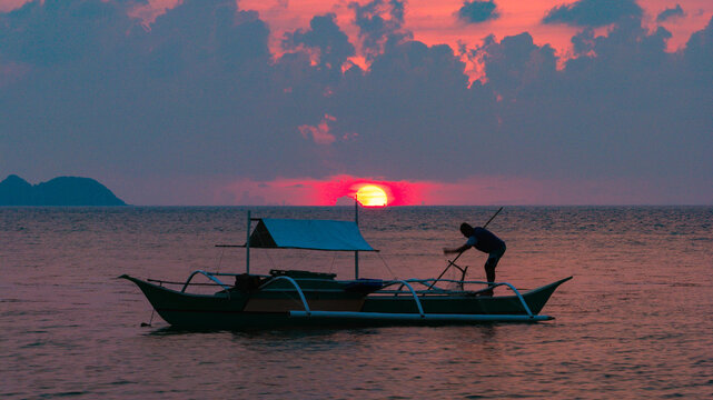 Aerial view of a traditional outrigger boat with a fisherman working at sunset over the calm sea in Busuanga, Mimaropa, Philippines.