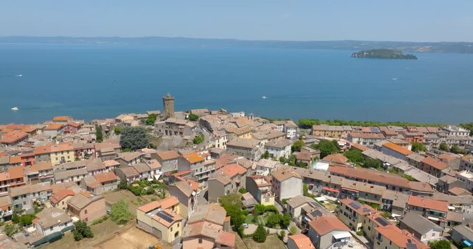 Panoramic aerial view of the historic center of Marta with the clock tower and old stone buildings overlooking Lake Bolsena, Martana island and hills beyond, in the province of Viterbo, Lazio, Italy.