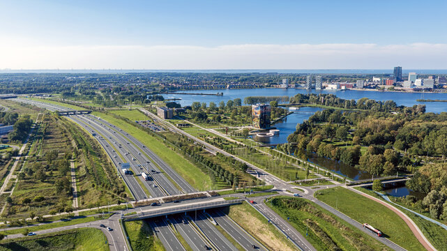Aerial view of the A6 highway stretching through green landscapes and urban areas near the Weerwater lake with the city skyline in the background in Almere, Flevoland, Netherlands.