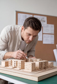An architect carefully cuts details on a wooden architectural model of a residential complex in his studio.