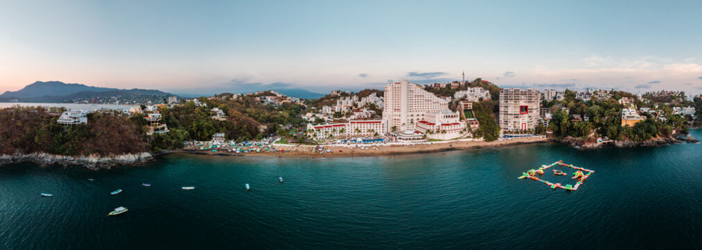 Aerial view of La Audiencia beach in Manzanillo, featuring luxury hotels, lush hillsides, and a floating water park in the Pacific Ocean, Manzanillo, Colima, Mexico.