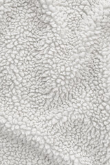 Detailed texture of white sherpa fleece fabric. Top view close-up of soft curly textile material for outerwear and interior design softly draped to create an abstract background © DariaR