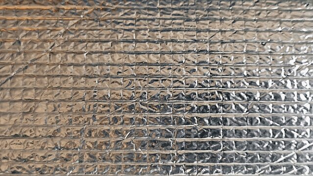 ​A close-up shot showing the textured surface of a thermal insulation foil sheet with a grid bubble wrap pattern