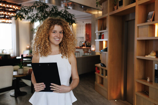 Smiling restaurant hostess holding clipboard in lobby