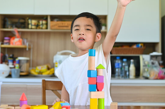 A young boy smiling and raising his hand while playing with colorful building blocks in a bright and inviting indoor environment of a home