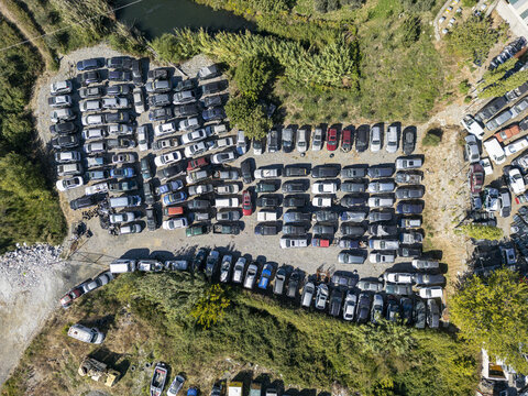 Aerial view of Pjese Auto Kledi, a car salvage yard filled with numerous parked vehicles arranged in rows on a gravel lot surrounded by greenery in Vau-Dejes, Shkoder County, Albania.